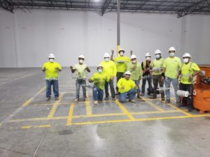 Alpha Insulation & Waterproofing employees wearing yellow shirts and white hard hats, standing together in a warehouse.