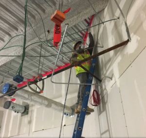 Technician standing on a ladder, installing firestopping solution in a commercial building.