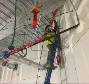 Technician standing on a ladder, installing firestopping solution in a commercial building.