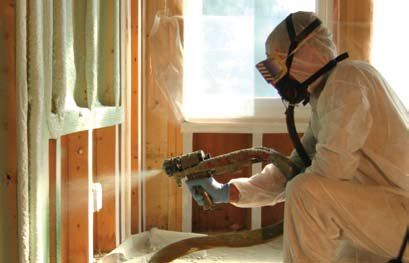 Technician in hazmat suit and gas mask, spraying spray foam insulation into an unfinished wall in a building.