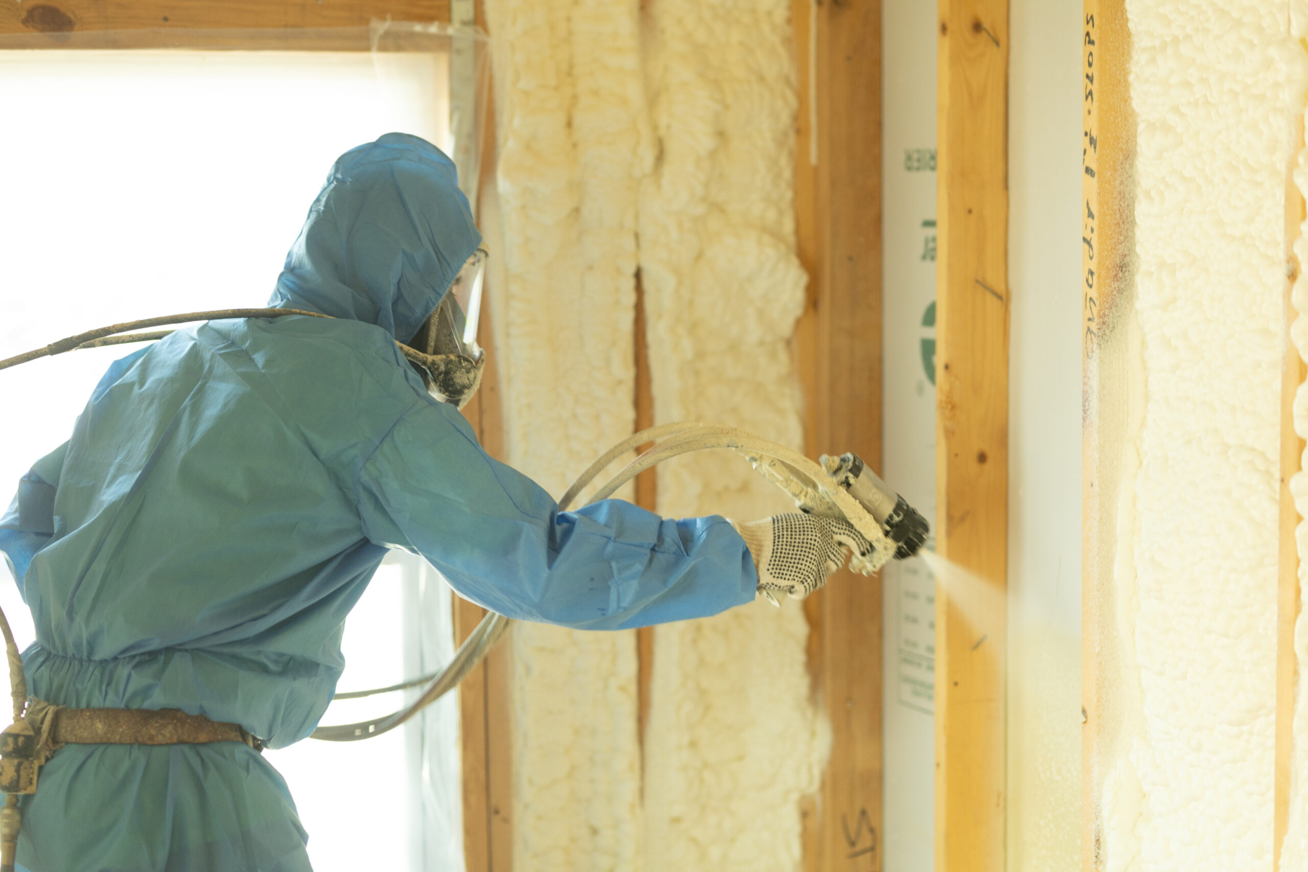 Technician in hazmat suit, installing spray foam insulation in a building's walls.